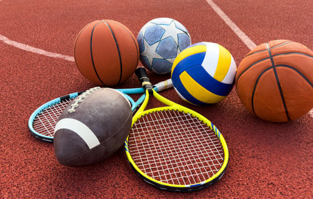 A variety of sports equipment including an american football, a soccer ball, a tennis racket, a tennis ball, and a basketballの写真素材