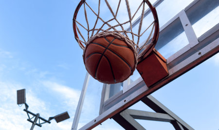Basketball ball and basketball hoop outdoors on sky background.