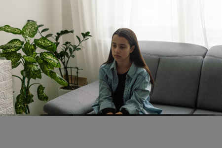 girl wearing blue shirt sitting on couch at home and looking away. Lifestyle child portrait.の写真素材