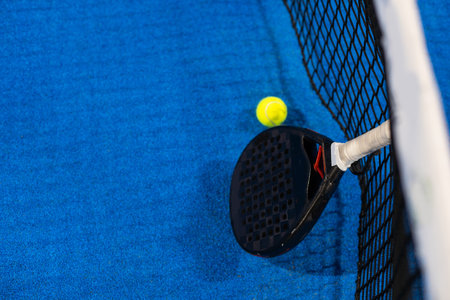 Black professional paddle tennis racket and ball with natural lighting on blue background. Horizontal sport theme poster, greeting cards, headers, website and appの写真素材