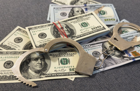 Financial crime, fraud, money laundering, corruption, or law enforcement : Bundles of US dollar 100 bills in a small case, alongside a pair of handcuffs placed over the US dollar currency.の写真素材
