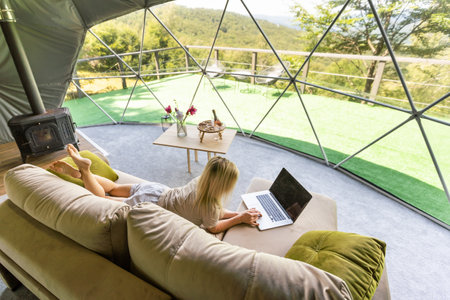 Happy young woman chatting online by using laptop in dome camping. Glamping vacation conceptの写真素材