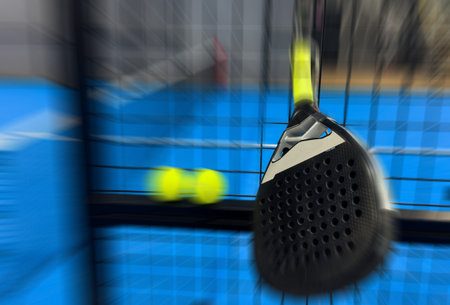 A padel or paddle tennis racket and a bright yellow tennis ball lie on a blue court.の写真素材