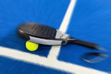 A padel or paddle tennis racket and a bright yellow tennis ball lie on a blue court.の写真素材