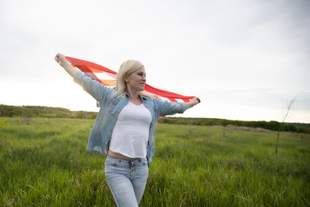 attractive woman holding a flag in the wind in a field. Summer landscape against the blue sky....