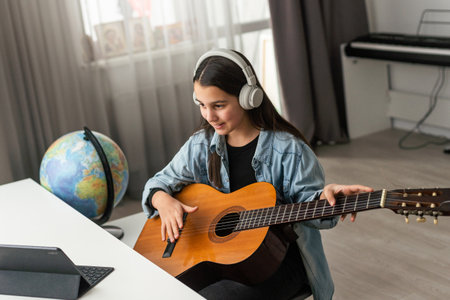 Girl with headphones listening to her online music lessons. Artistic kid playing the acoustic guitar and learning the chordsの写真素材