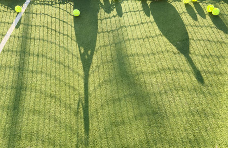 A tennis ball lies on a green court. The net and a blurred figure of a player are visible in the background.の写真素材