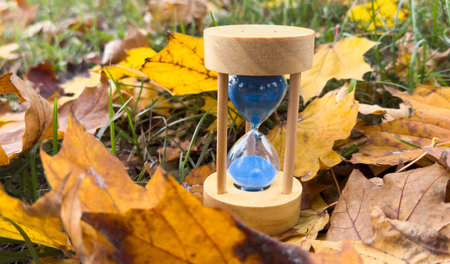 A blue sand clock is sitting on the ground in a field of fallen brown leaf. Concept of fall season...