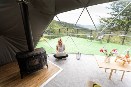 Happy young woman chatting online by using laptop in dome camping. Glamping vacation conceptの写真素材
