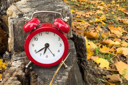 Traditional alarm clock on a background of orange and yellow maple leaves, fall time change conceptの写真素材
