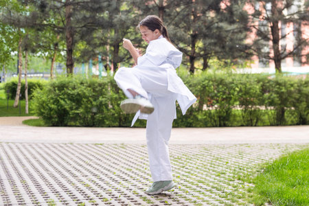 Young active girl wearing white kimono with white belt performing martial arts kick skills. Sporty karate woman improving fight technique.の写真素材