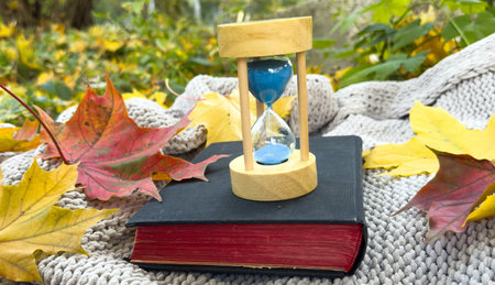 Hourglass Indicating Passing Time Beside a Book and Autumn Leafの写真素材