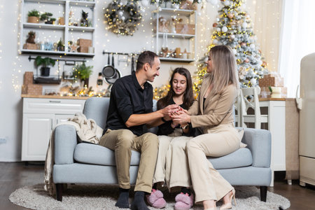 festive girl opening xmas gifts on Christmas eve with mom and dad, decorated kitchen interior, copy spaceの写真素材