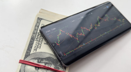Stock exchange on smartphones screen and dollars banknotes blurred