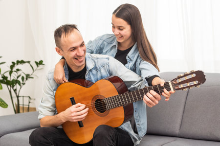 Father guy teaching girl teenager daughter guitar playing at home. Family musical lessons with strings instrumentの写真素材