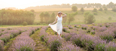 Beautiful young woman wearing a white dress walking in the middle of a lavender field in bloomの写真素材