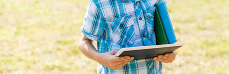 Happy child sitting on the field holding tablet. Boy sitting on the grass on sunny day. Home schooling or playing a tabletの写真素材