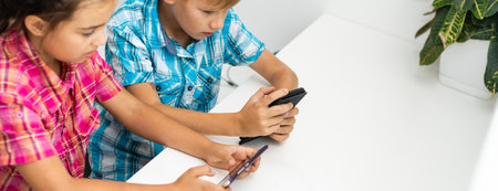 Education, friendship, technology and people concept. children using mobile phone, pointing fingers, while sittingの写真素材