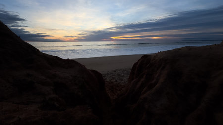 Beautiful sandy beach with red rocks and cliffs. Sunset at dusk with shallow waves on the Atlantic...