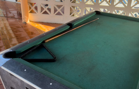 Close up of a rustic wooden triangle pool rack and worn billiard cue stick resting on an old, dusty...