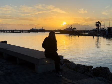 Vilamoura Marina, Algarve, Portugal at sunset, a line of boats and yaghts moored against a jetty, the sky and the water are lit bright orange by the setting sunの写真素材