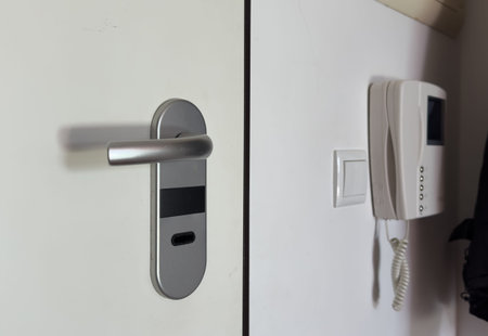 A white wall with an intercom hanging on the wall, a light-on button and an armored door