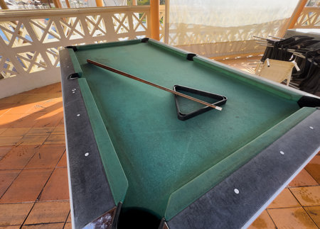 Close up of a rustic wooden triangle pool rack and worn billiard cue stick resting on an old, dusty...