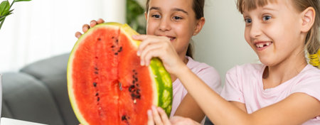 Two smiling girls are holding watermelon in their hands. Kids eat fruit indoor. Healthy snack for children. Kids enjoying watermelon. Happy childhood. Space for textの写真素材