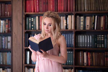a blonde girl with 2 pigtails on the background of a bookshelf with an open book in her hands in a photo Studioの写真素材