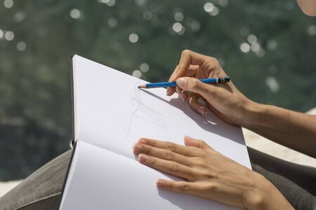 Woman hands drawing a sketch on a white page of a sketchbook, using a blue 6B pencil, Outdoorsの写真素材