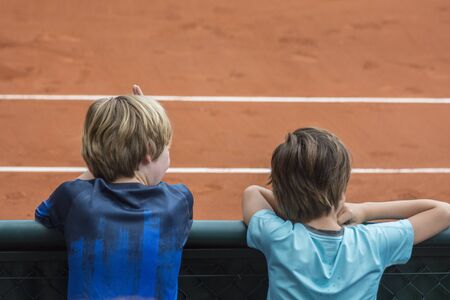 Two kids, facing backwards, watching a Tennis game in a clay court, during the French open tournamentの写真素材