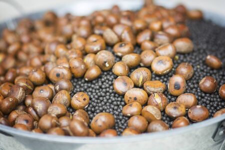 Close up view of roasted Chestnuts (Castanea sativa) in a metal ball with black sand.  Chengdu, Sichuan, Chinaの写真素材