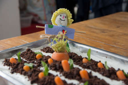 Homemade Carrot cake shaped as a carrot garden, decorated with a scarecrow doll, with topping of chocolate "soil" and mini carrots.の写真素材