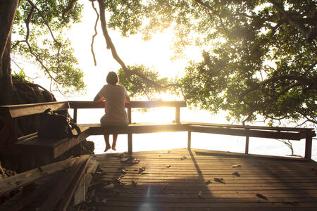 woman sitting on bench at ocean front,の写真素材