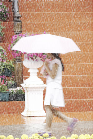 Little Asian girl having fun in the rain with her umbrellaの写真素材