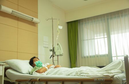 An adult woman in a hospital recovery bed wearing a mask.の写真素材