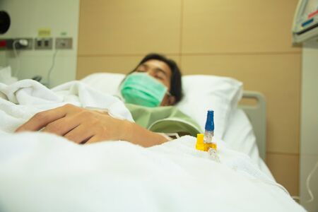 Patient lies in hospital bed with drip equipment in foreground. Focus is on the dripの写真素材