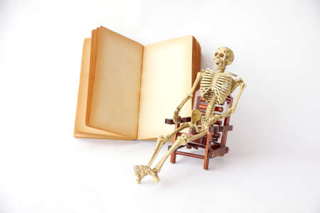 Human skeleton Sit on a chair With old books on white backgroundの写真素材