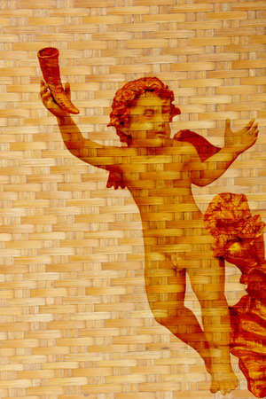 Stock Photo - cupid statue with gold color wing on texture of bamboo weaveの写真素材