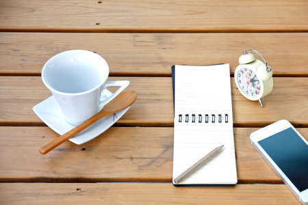 empty cup of coffee on a wooden table with smartphone and notebook and pencil. Simple workspace or coffee breakの写真素材