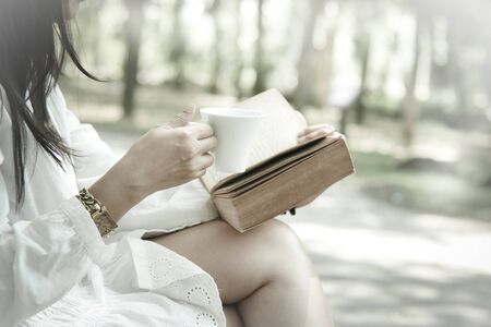 Woman sitting on the park reading a book holding her coffee mug soft focus vintage styleの写真素材
