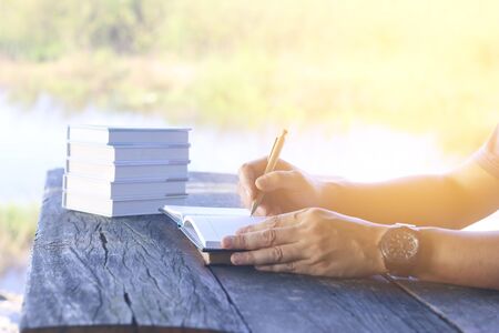 man right hand writing journal on small notebook at outdoor area with morning sceneの写真素材