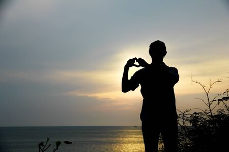 Silhouette hand in heart shape with sunrise in the beach backgroundの写真素材