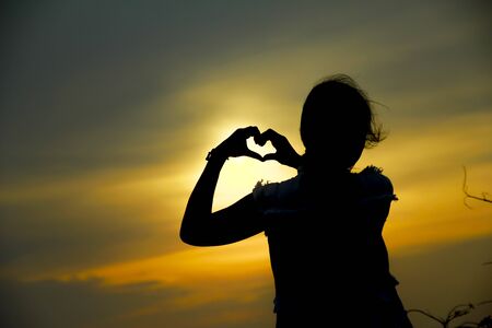 heart shape made with a girl hands at sunsetの写真素材