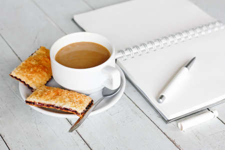 Breakfast with coffee and fresh strawberry pie with open  notepad and pen on vintage white wooden tableの写真素材
