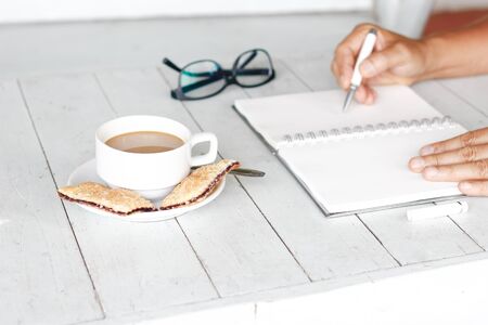Cropped image of a man sitting at vintage white wooden table and coffee while working with notepadの写真素材
