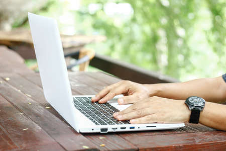 Close up low angle view of a man working on a laptop computer sitting on wooden table with blur...