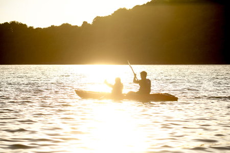 Sunset Reflections on the Water with Kayakers Silhouetted on a Yellow Orange Background of Water and Skyの写真素材
