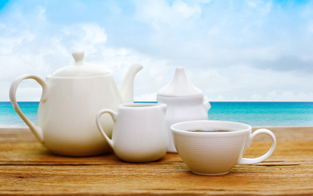Cup and pot of tea on the wooden table on Beautiful tropical beach and sea with white cloud and blue sky background - Holiday Vacation conceptの写真素材