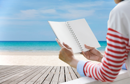 Young woman reading a book View from rear.on beautiful tropical beach and sea with white cloud and blue sky background - Holiday Vacation conceptの写真素材